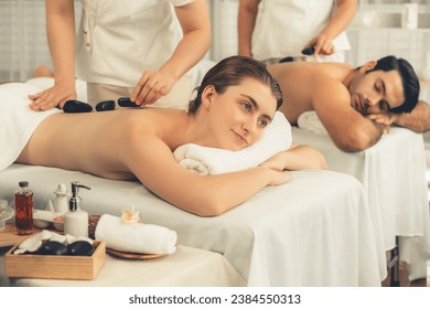 Hot stone massage at spa salon in luxury resort with day light serenity ambient, blissful couple customer enjoying spa basalt stone massage glide over body with soothing warmth. Quiescent - Powered by Shutterstock