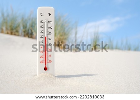 Hot summer day. Celsius and fahrenheit scale thermometer in the sand. Ambient temperature plus 22 degrees 