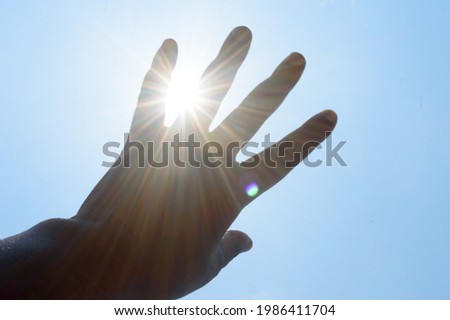 Hot summer sunlight rays pouring through human hand. Hand covering sun light heat temperature. 