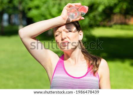 hot summer weather. girl covering her head from sunshine with hand in pain. young woman with bottle of water from thirst on sun. female female go sports get heat and sunstroke. Headache, feeling bad