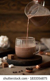 hot sweet chocolate cocoa is poured into a glass cup on a wooden table