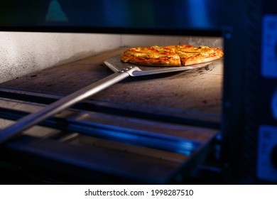 Hot Tasty American Pizza With Tomato Cheese And Meat With A Thick Crust On A Metal Shovel, The Baker Takes Out The Pizza From The Oven