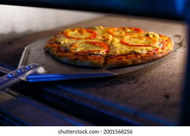 Hot Tasty American Pizza With Tomato Cheese And Meat With A Thick Crust On A Metal Shovel, The Baker Takes Out The Pizza From The Oven