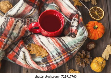 Hot tea cup with cozy scarf, autumnal feeling setting on old wooden board with fall decoration ornaments and dried leaves