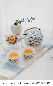 Hot tea in a fine ceramic teapot and cup or earl grey tea on the white table with crispy rice snack in the white window light ambient background - Shutterstock ID 2060160890