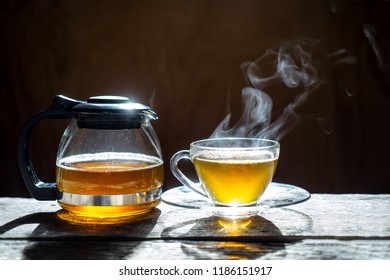 Hot Tea In Glass Teapot And Cup With Steam On Wood Background