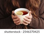 Hot tea in a mug. Woman holding mug of lemon tea. Cold winter relax background. Woolen sweater warm clothing. Long hair girl. Cozy atmosphere. Female hands holding tea.