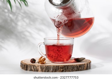 Hot tea is pouring from glass teapot into cup. Hibiscus red tea in glass cup close-up view