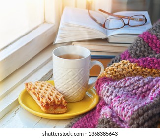 A сup of hot tea, stack of books, glasses and cookie on the background of a knitted blanket.
