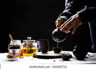 Hot tea in a teapot, glass and cup on a black background and hands pouring tea