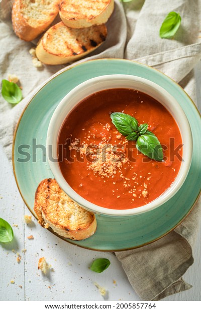 Hot tomato soup with toasts and\
basil. Soup with parmesan Red tomato soup in blue\
pottery.