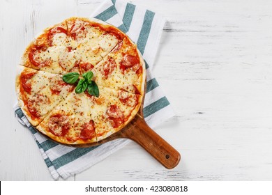 Hot true PEPPERONI ITALIAN PIZZA on towel with salami and cheese. TOP VIEW Tasty traditional pepperoni pizza on board on white wooden table. Copy space for your logo. Ideal for commercial 