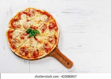 Hot true PEPPERONI ITALIAN PIZZA with salami and cheese. TOP VIEW Tasty traditional pepperoni pizza on board on white wooden table. Copy space for your logo. Ideal for commercial 