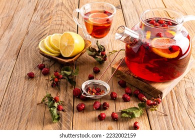 hot vitamin tea with rose hips stands on a wooden podium and a table with a cup of tea and lemon slices. phytotherapy. anti-cold drinks
