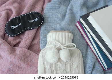 A Hot Water Bottle, An Eye Mask And A Pile Of Books On A Bed. Top View, Hygge, Winter. 