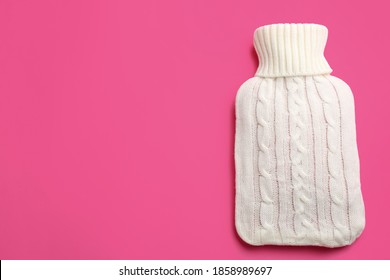 Hot water bottle with knitted cover on pink background, top view. Space for text