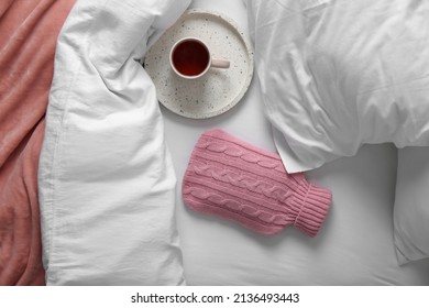 Hot Water Bottle With Knitted Cover And Cup Of Tea On Bed, Flat Lay