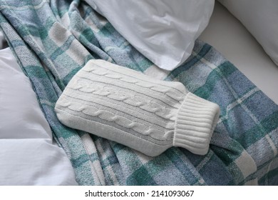 Hot Water Bottle With Knitted Cover And Checkered Plaid On Bed