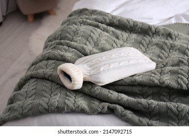 Hot Water Bottle With Knitted Cover On Bed Indoors