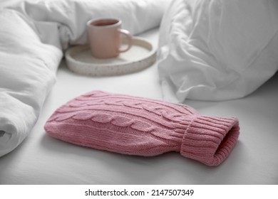 Hot Water Bottle With Knitted Cover And Cup Of Tea On Bed