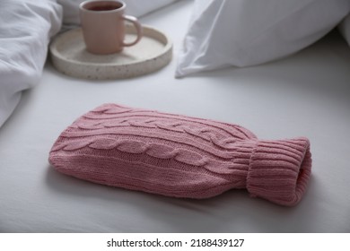 Hot Water Bottle With Knitted Cover And Cup Of Tea On Bed