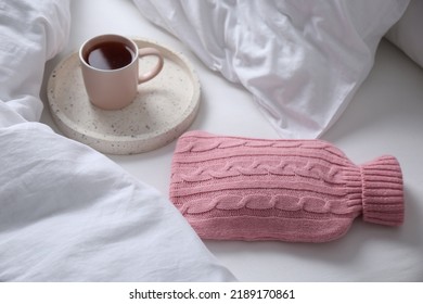 Hot Water Bottle With Knitted Cover And Cup Of Tea On Bed