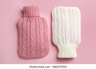 Hot water bottles with knitted covers on pink background, flat lay