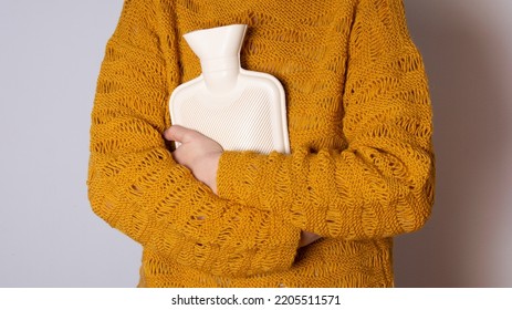 Hot water heating pad is winter essentials.  Power outages and difficulties with heating. Saving electricity. Woman in orange sweater holding heating pad. - Powered by Shutterstock