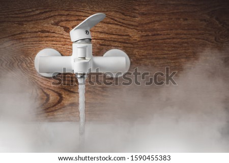 Hot water runs from the white tap. Steam rises up above the water