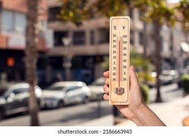 Hot weather. Thermometer in hand in front of an urban scene during heatwave.  - Powered by Shutterstock