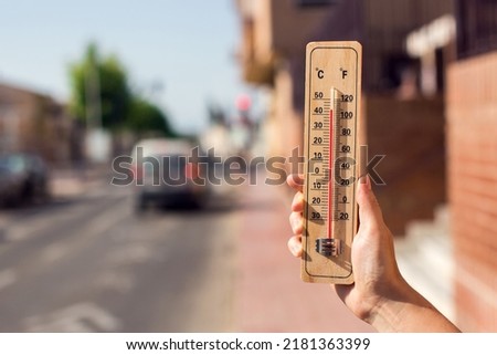 Hot weather. Thermometer in hand in front of an urban scene during heatwave. 