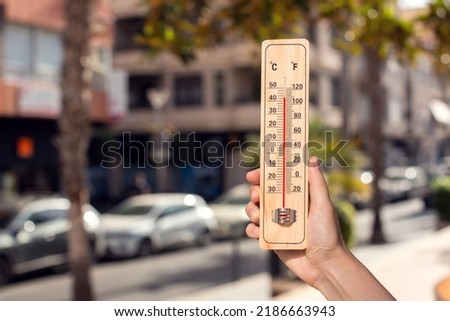Hot weather. Thermometer in hand in front of an urban scene during heatwave. 
