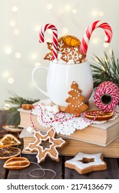Hot winter drink in a white mug: cozy home composition with homemade gingerbread cookies, candy cane, fir tree branch. Wooden background, christmas lights and candles - Shutterstock ID 2174136679