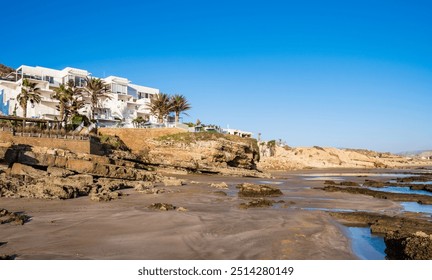 Hotel complex on cliff at La Source beach in Taghazout near Agadir, Morocco. Rugged rocky coastline of Atlantic ocean attracts surfers and tourists. Famous surf spot. - Powered by Shutterstock