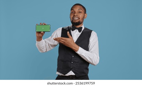 Hotel concierge personnel showing chroma key display on a smartphone, posing with hospitality industry uniform in studio. Doorkeeper lounge area staff shows green screen. Camera B. - Powered by Shutterstock