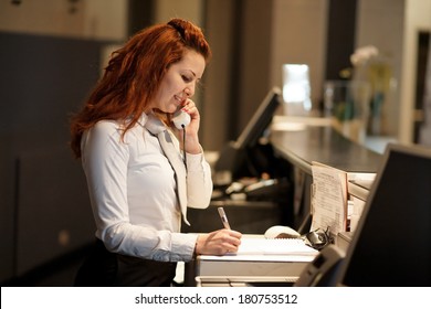 Hotel Concierge .Reception Of Hotel, Desk Clerk, Woman Taking A Call And Smiling.