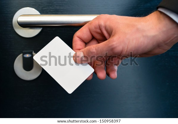 Hotel door - Young man holding a\
keycard in front of the electronic sensor of a room door\
