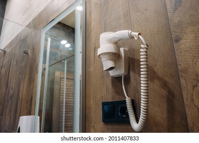 Hotel Hand Held Hair Dryer On Dark Wall. There Is A Mirror In The Background.