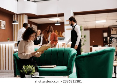 Hotel manager checking record files in lobby lounge area, reviewing registration forms and bureaucracy reports. Young resort administrator sitting on couch to ensure excellent service. - Powered by Shutterstock