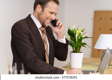 Hotel Manager Checking A Reservation On His Computer As He Talks On The Phone With A Prospective Client