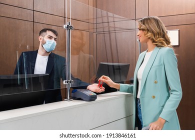 Hotel Manager In Medical Mask Giving Key To Young Woman In Lobby
