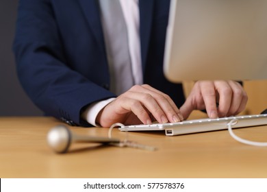 Hotel Manager Typing On A Computer Entering Client Data With A Room Key Lying On The Counter In Front Of Him