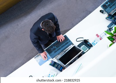 Hotel Receptionist Working On Computer At Front Desk Office