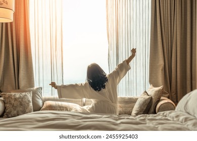 Hotel relaxation on lazy day with Asian woman waking up from good sleep on bed in weekend morning resting in comfort bedroom looking toward city view, having happy, work-life quality balance lifestyle - Powered by Shutterstock