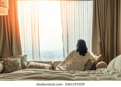 Hotel relaxation on lazy day with Asian woman waking up from good sleep on bed in weekend morning resting in comfort bedroom looking toward city view, having happy, work-life quality balance lifestyle - Powered by Shutterstock