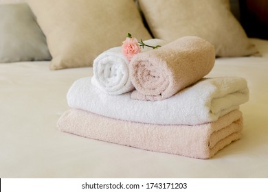 Hotel room with freshly made bed, perfectly clean and ironed sheets, stack of new folded towels and single flower as decoration in natural sun light. Close up, copy space for text. - Shutterstock ID 1743171203