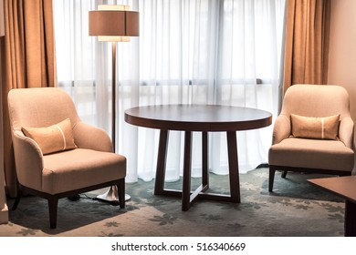 Hotel room interior. Coffee table, two armchairs with pillows and floor lamp on the carpet in front of the window.