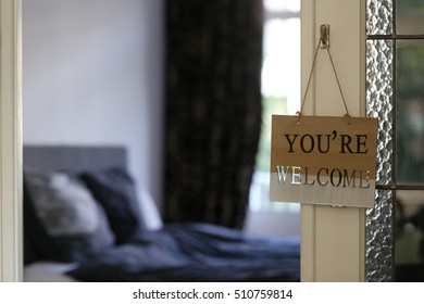 Hotel room, You are welcome words on wooden vintage frame card background, hanging on the bedroom door, enter the home. Welcoming hotel bed with pillows and backlight from the window.  - Shutterstock ID 510759814