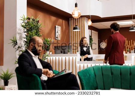 Hotel staff greeting businessman travelling on work trip, friendly receptionist ensuring easy check in process and pleasant stay at luxury resort. Young man in suit meeting employee at front desk. Foto stock © 