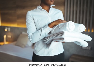 Hotel staff setting up pillow on bed. African housekeeper looking at the camera holding a towel a hotel room. Clean towels during housekeeping in a hotel room